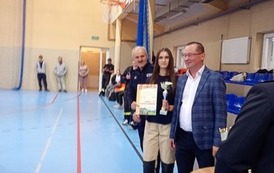 Zdjęcia przedstawiają uczestnik&oacute;w w strojach sportowych i strażackich podczas rywalizacji na hali sportowej, m.in. dynamiczne konkurencje z wężami strażackimi, uroczystą zbi&oacute;rkę wszystkich drużyn, a także momenty wręczania puchar&oacute;w, dyplom&oacute;w oraz nagr&oacute;d indywidualnych przez zaproszonych gości i przedstawicieli straży pożarnej.