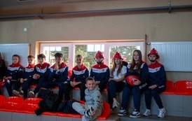 Zdjęcia przedstawiają uczestnik&oacute;w w strojach sportowych i strażackich podczas rywalizacji na hali sportowej, m.in. dynamiczne konkurencje z wężami strażackimi, uroczystą zbi&oacute;rkę wszystkich drużyn, a także momenty wręczania puchar&oacute;w, dyplom&oacute;w oraz nagr&oacute;d indywidualnych przez zaproszonych gości i przedstawicieli straży pożarnej.