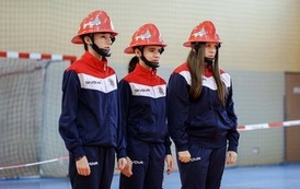 Zdjęcia przedstawiają uczestnik&oacute;w w strojach sportowych i strażackich podczas rywalizacji na hali sportowej, m.in. dynamiczne konkurencje z wężami strażackimi, uroczystą zbi&oacute;rkę wszystkich drużyn, a także momenty wręczania puchar&oacute;w, dyplom&oacute;w oraz nagr&oacute;d indywidualnych przez zaproszonych gości i przedstawicieli straży pożarnej.