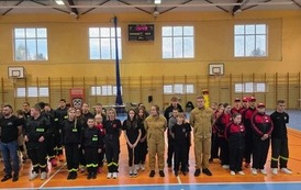 Zdjęcia przedstawiają uczestnik&oacute;w w strojach sportowych i strażackich podczas rywalizacji na hali sportowej, m.in. dynamiczne konkurencje z wężami strażackimi, uroczystą zbi&oacute;rkę wszystkich drużyn, a także momenty wręczania puchar&oacute;w, dyplom&oacute;w oraz nagr&oacute;d indywidualnych przez zaproszonych gości i przedstawicieli straży pożarnej.