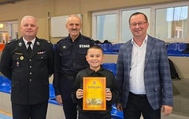Zdjęcia przedstawiają uczestnik&oacute;w w strojach sportowych i strażackich podczas rywalizacji na hali sportowej, m.in. dynamiczne konkurencje z wężami strażackimi, uroczystą zbi&oacute;rkę wszystkich drużyn, a także momenty wręczania puchar&oacute;w, dyplom&oacute;w oraz nagr&oacute;d indywidualnych przez zaproszonych gości i przedstawicieli straży pożarnej.