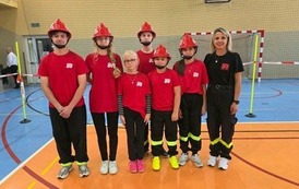 Zdjęcia przedstawiają uczestnik&oacute;w w strojach sportowych i strażackich podczas rywalizacji na hali sportowej, m.in. dynamiczne konkurencje z wężami strażackimi, uroczystą zbi&oacute;rkę wszystkich drużyn, a także momenty wręczania puchar&oacute;w, dyplom&oacute;w oraz nagr&oacute;d indywidualnych przez zaproszonych gości i przedstawicieli straży pożarnej.