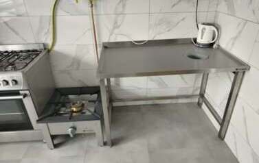 Zdjęcie przedstawiające wyposażenie kuchni, metalowe, nierdzewne elementy takie jak p&oacute;łki, st&oacute;ł sprzęt AGD. 