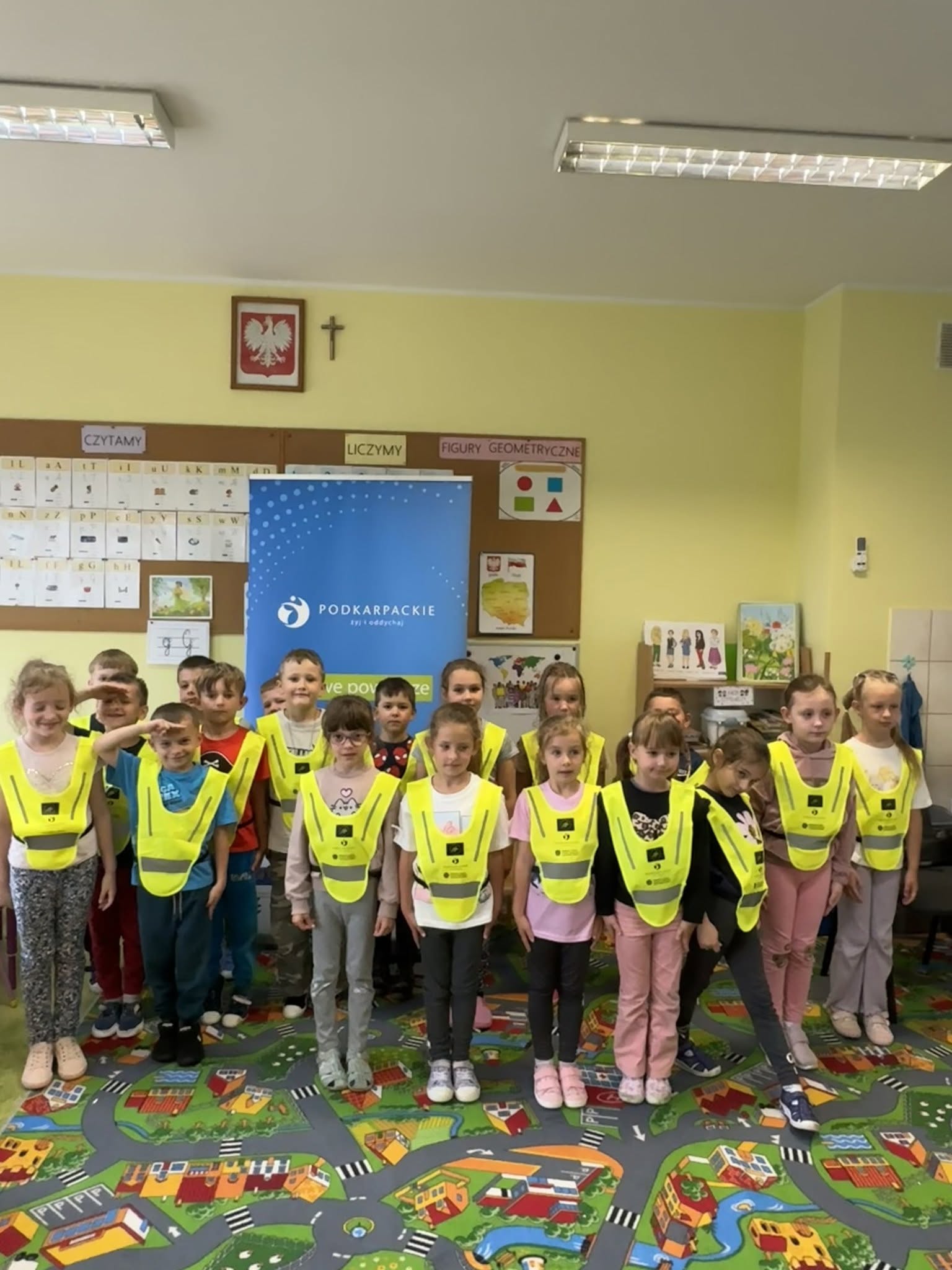 Grupowe zdjęcie przedszkolak&oacute;w w&nbsp;odblaskowych kamizelkach. 