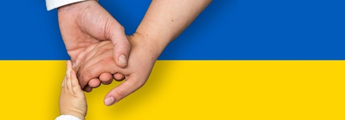 Flaga Ukrainy niebiesko- żółta a na niej widoczne dłonie męska, żeńska i dziecięca. Dłonie splecione. 