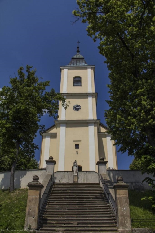 Kościół Parafialny w Kobylanach. Zdjęcie wysokiego budynku, a także murowanego ogrodzenia. 
