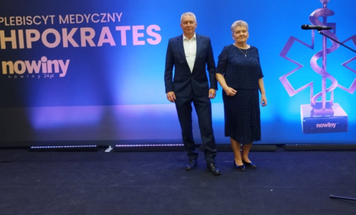 Dwie elegancko ubrane osoby stoją na scenie podczas uroczystej gali medycznej.  W tle widoczny jest baner z napisem „Plebiscyt Medyczny HIPOKRATES” oraz logo „no