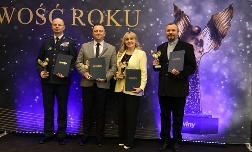 Różnorodność i jedność w działaniu na rzecz dobra wspólnego: Małgorzata Wierdak stoi na tle ścianki obok innych laureatów, w tym funkcjonariusza policji w galowym mundurze, mężczyzny w garniturze i księdza. Wszyscy trzymają trofea, co symbolizuje, że wyró