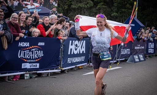 Katarzyna Dombrowska wbiega na metę z biało-czerwoną flagą dumnie uniesioną nad głową. Na jej twarzy maluje się ogromne wzruszenie i radość, a wzdłuż barier szpaler kibiców bije brawo.
